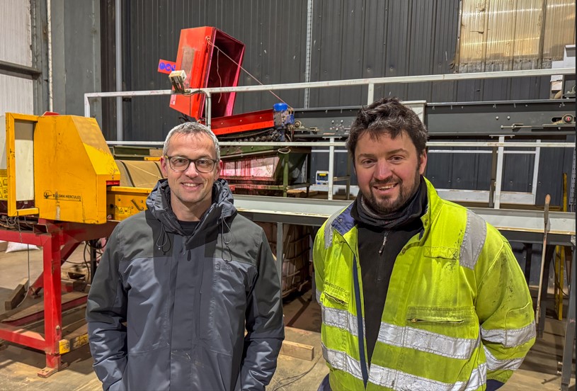 Two men in front of red machine, one wearing hi-viz vest