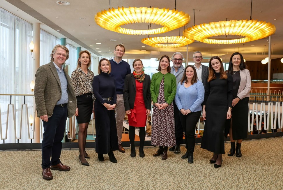 Group photo of ten professionally dressed people standing in a modern interior with large windows and distinctive circular ceiling lights.