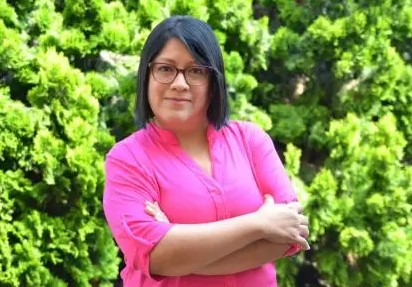 Lady with black bobbed hair wearing pink blouse in front of hedge