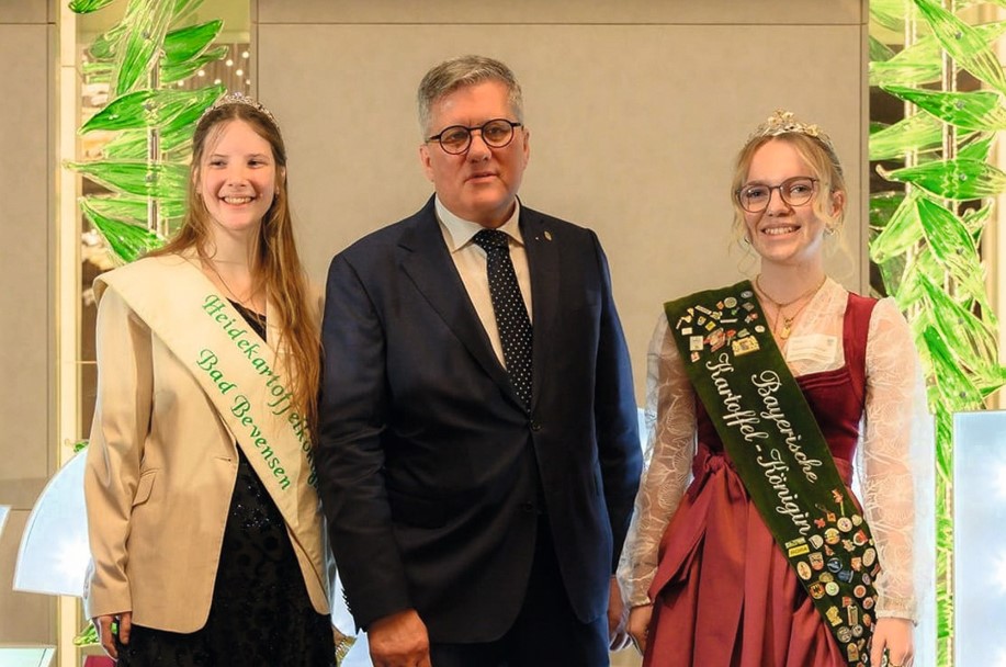 Two attractive young women wearing formal wear and sashes either side of a man in suit and tie