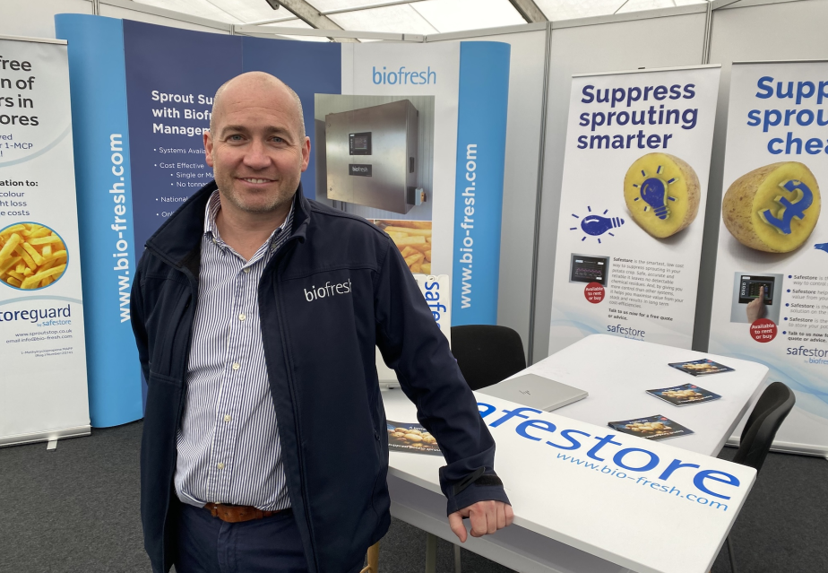Man in front of trade stand with text and photos of potatoes on posters