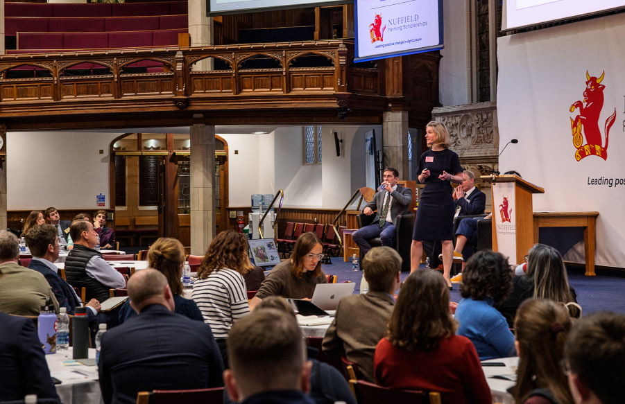 Lady in front of projector screen addressing room full of scholars