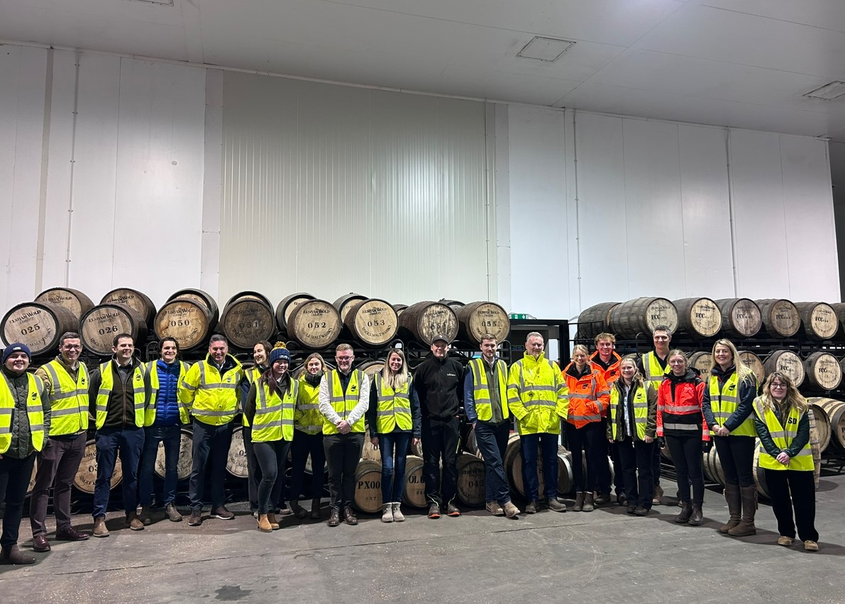 Young people in high viz jackets inside factory with wooden containers behind them