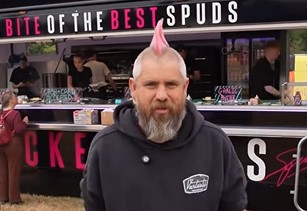 Man with pink mohican hair in front of baked potato stand