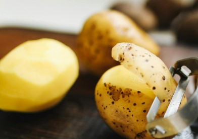 Three potatoes, one peeled, one with peel and one being peeled