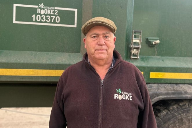 Man in fleece and flat cap standing in front of agricultural delivery lorry