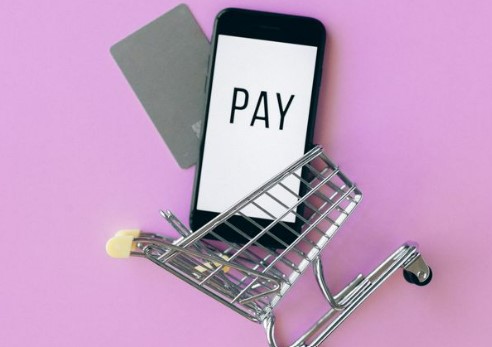 mobile phone and payment card in miniature shopping trolley on pink background